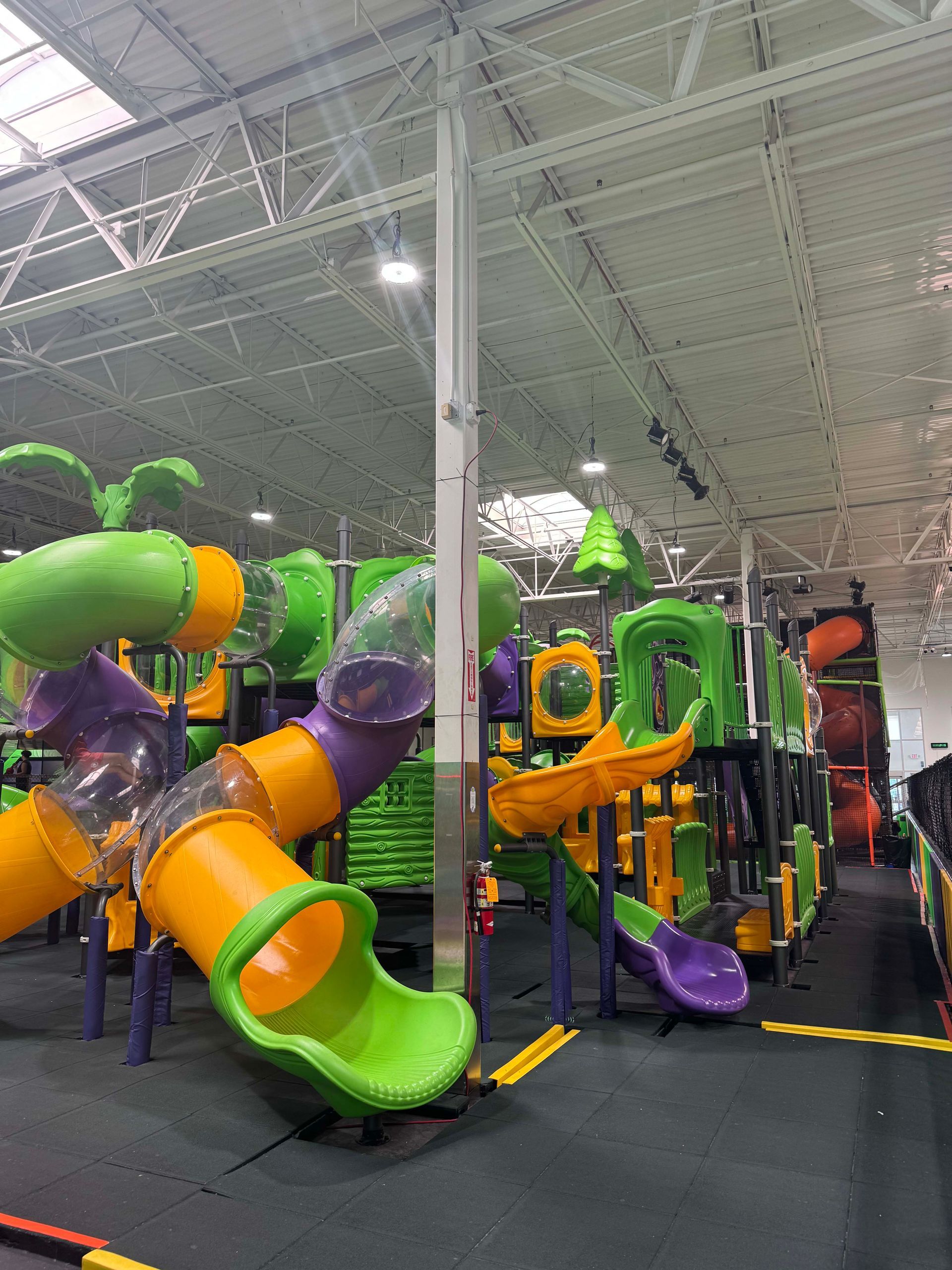 Indoor playground with colorful slides and climbing structures under a high ceiling