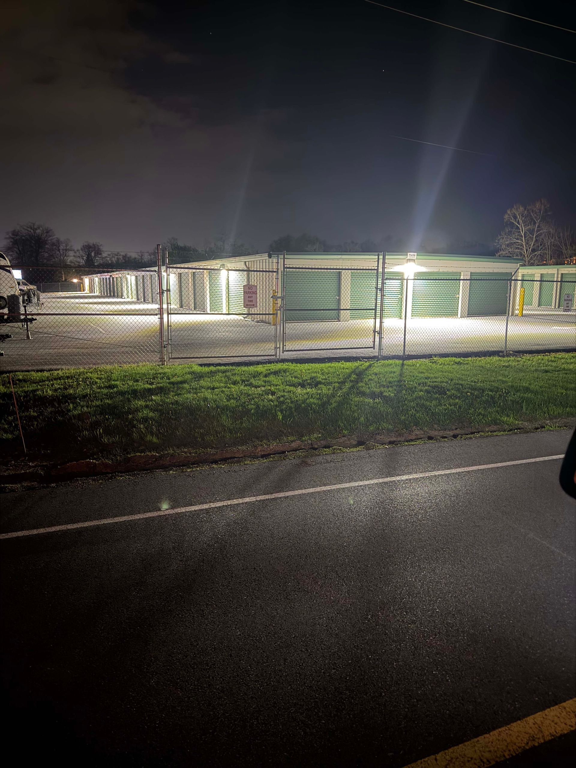 Nighttime view of a lit building with green walls behind a wet road and grassy verge