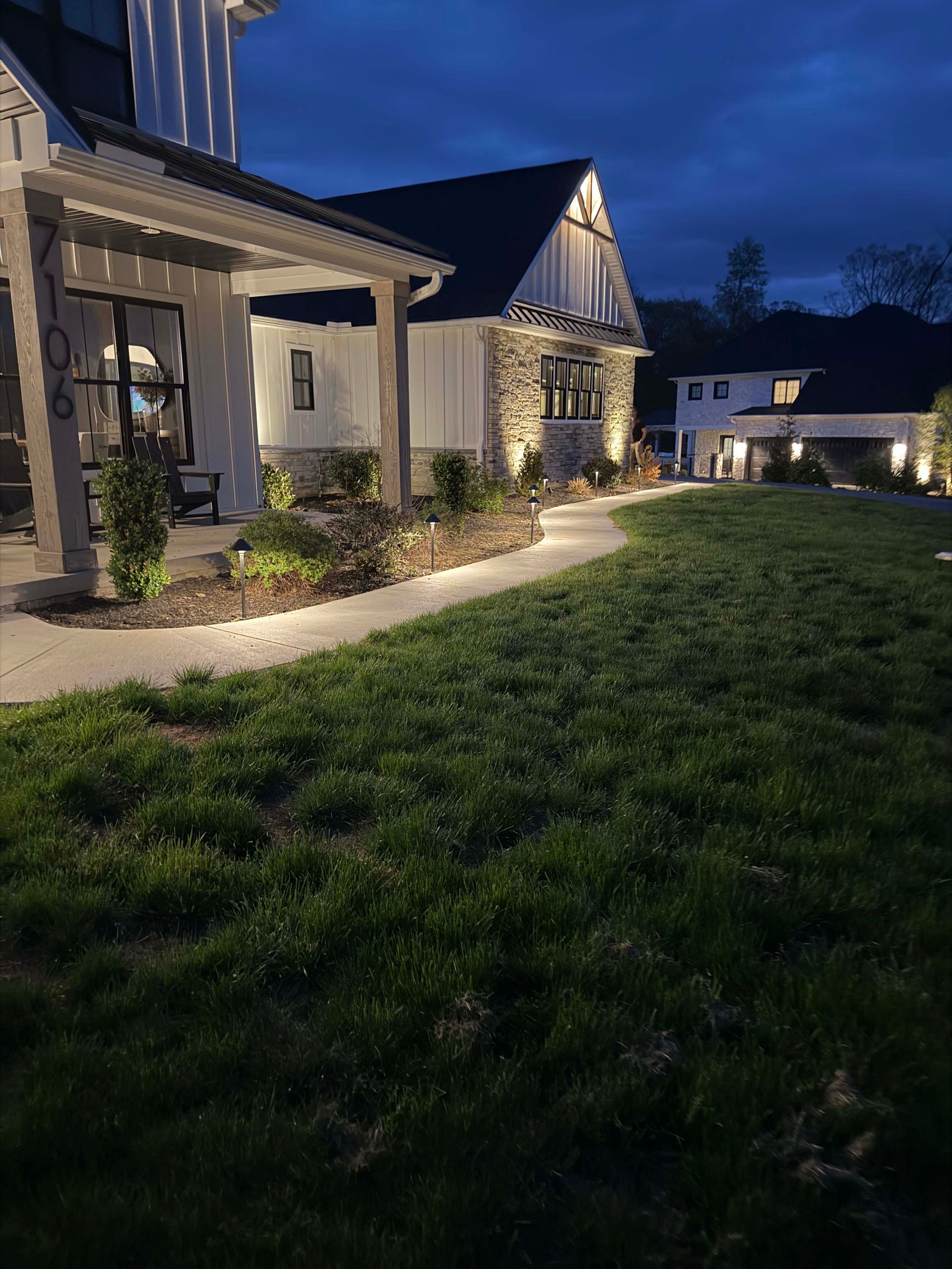 Modern house exterior at dusk with lit windows, landscaped lawn, and pathway lights