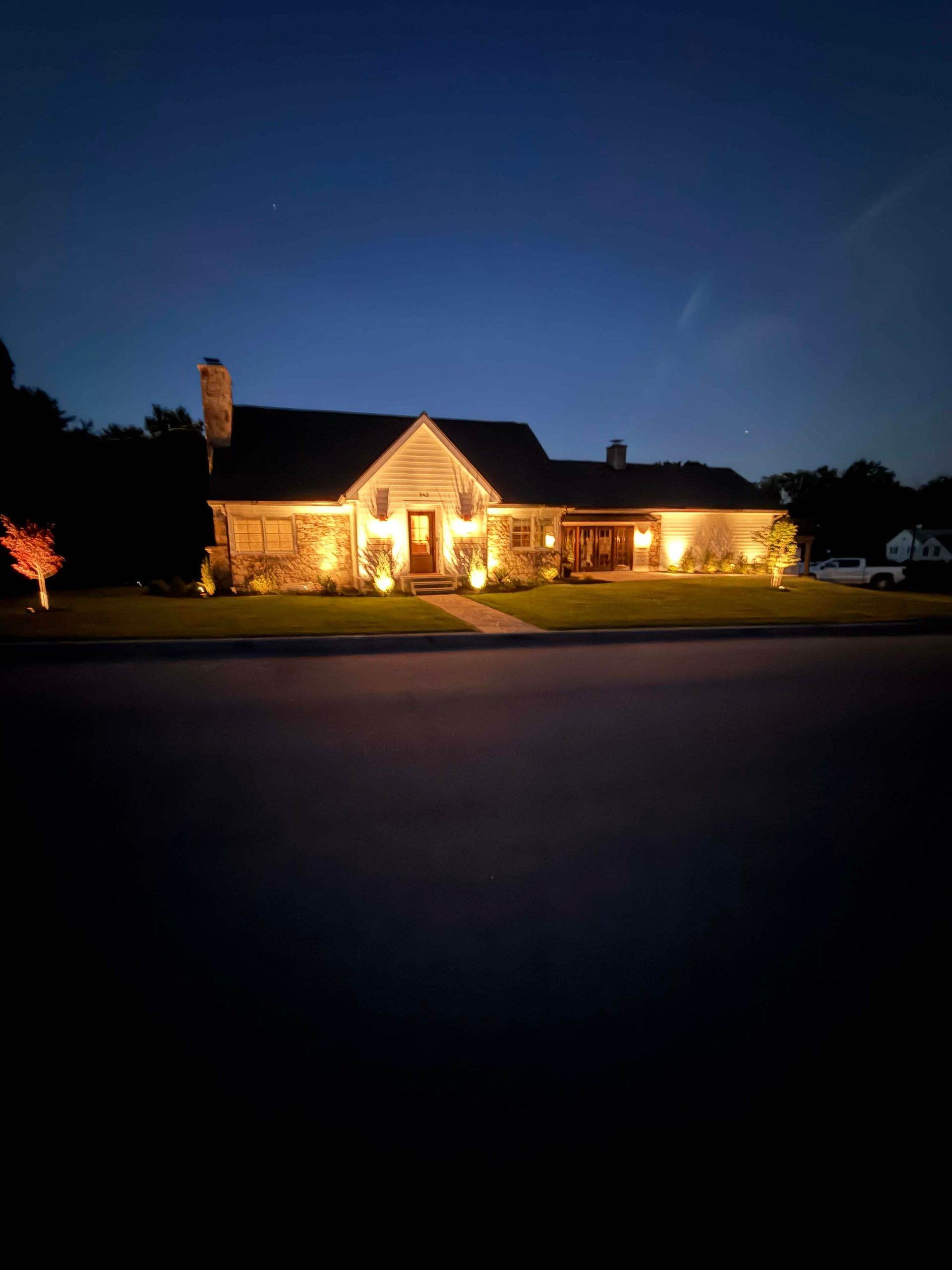 Well-lit house at dusk with warm porch lights and a dark blue evening sky