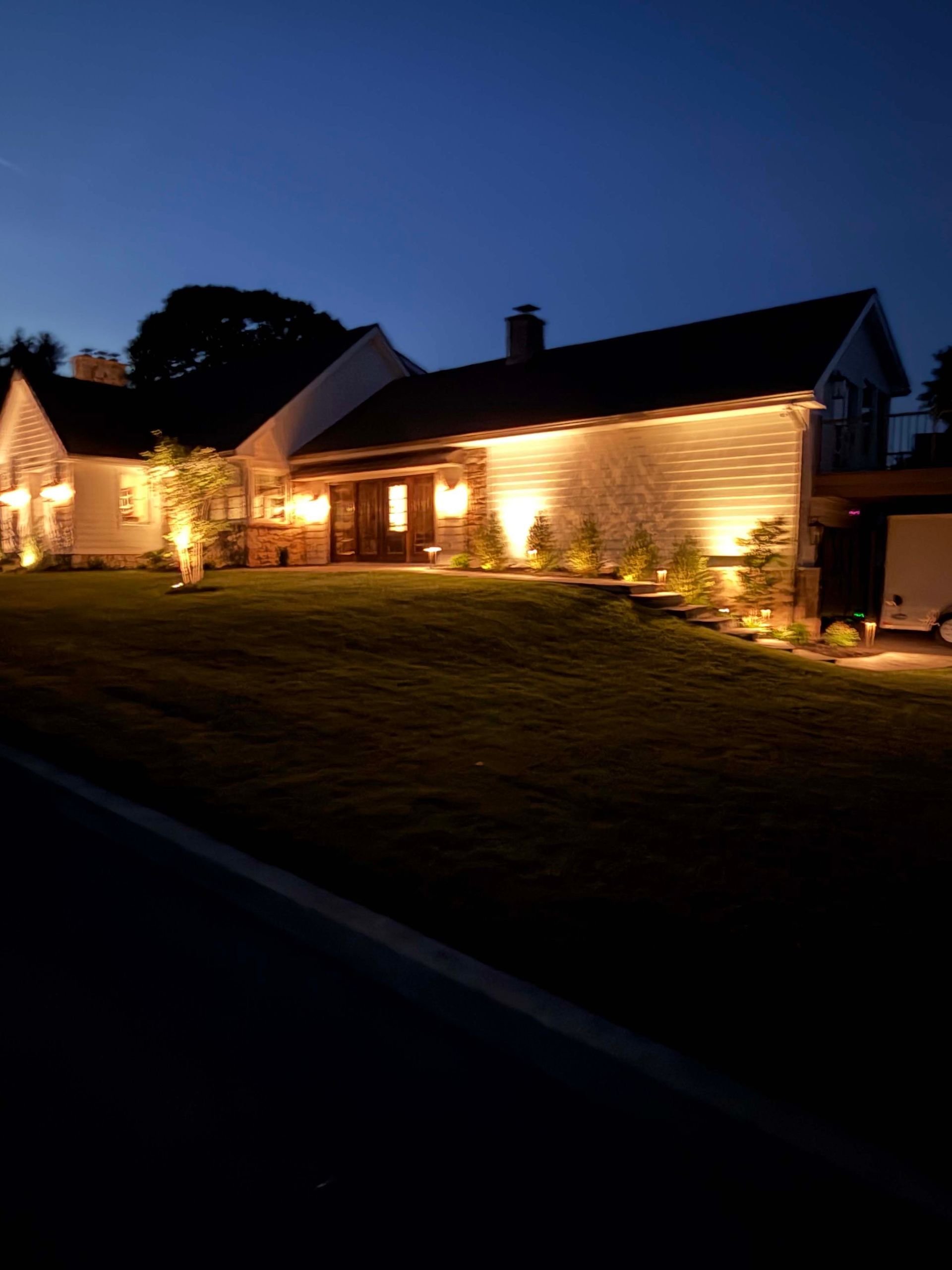 Single-story house warmly lit at dusk, with lights along the exterior and a dark blue evening sky.
