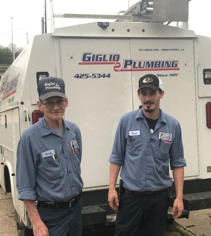 Two plumbers standing in front of a white service truck with “Plumbing” signage.