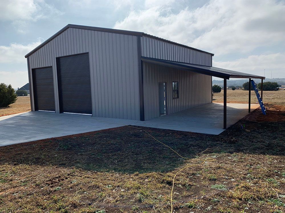 A metal building with a porch and garage doors is sitting in the middle of a field.