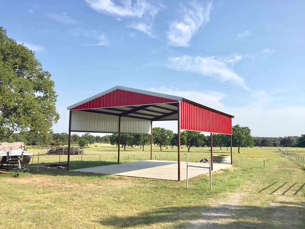 A red and white metal shed is sitting in the middle of a grassy field.