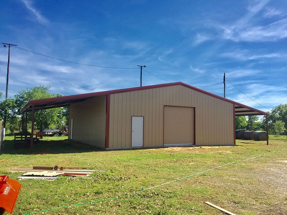 A large metal building with a red roof is sitting in the middle of a grassy field.