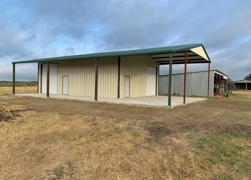 A large metal building with a green roof is sitting in the middle of a field.