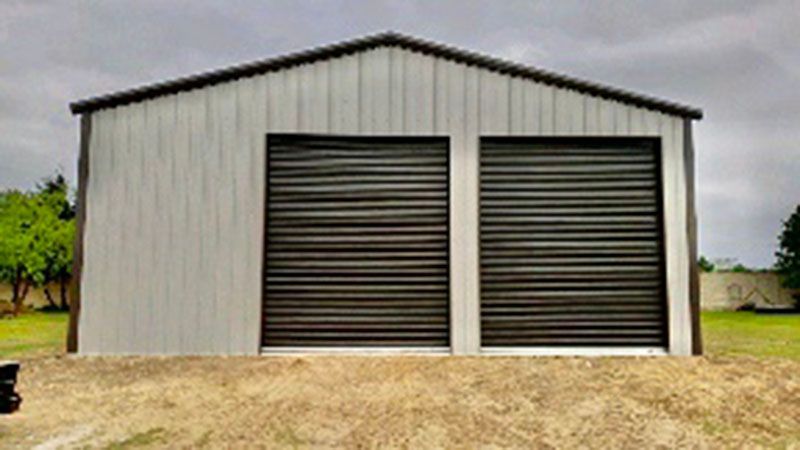 A metal garage with two black garage doors is sitting on top of a dirt hill.