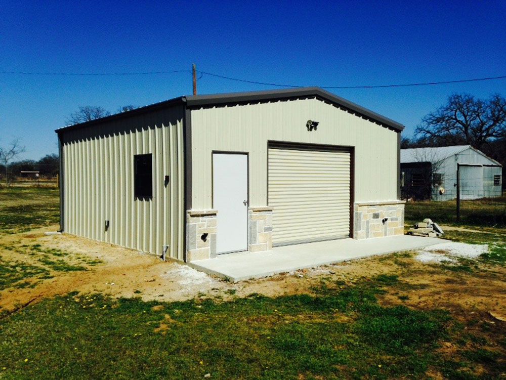 A metal building with a garage door is sitting in the middle of a grassy field.