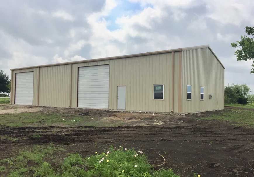 A large metal building is sitting in the middle of a dirt field.