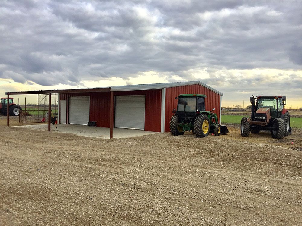 Two tractors are parked in front of a red barn.
