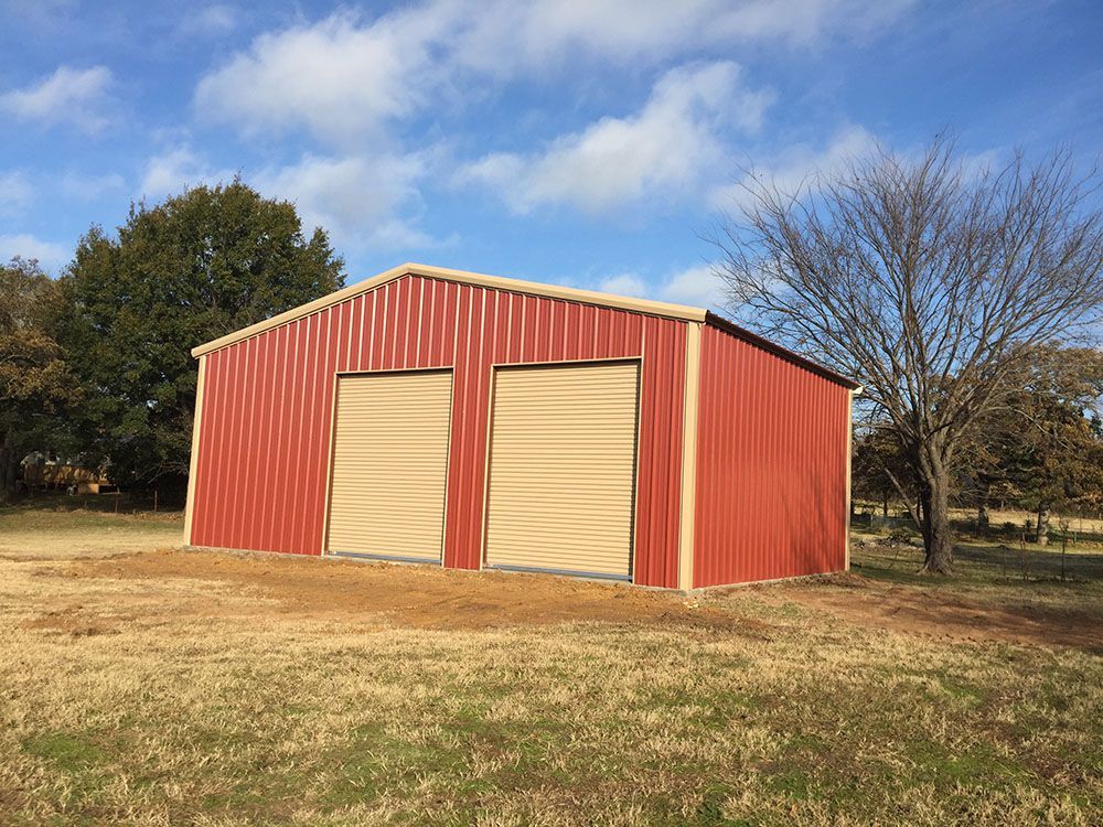 A red barn with two doors is sitting in the middle of a field.