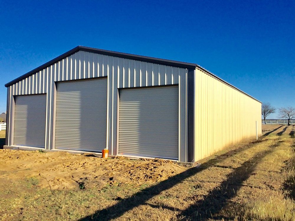 A large metal building with three garage doors is sitting in the middle of a field.