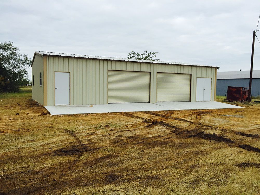 A large metal building with three garage doors in a field