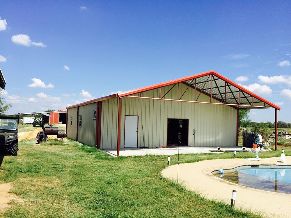 A large metal building with a red roof is sitting next to a pool.
