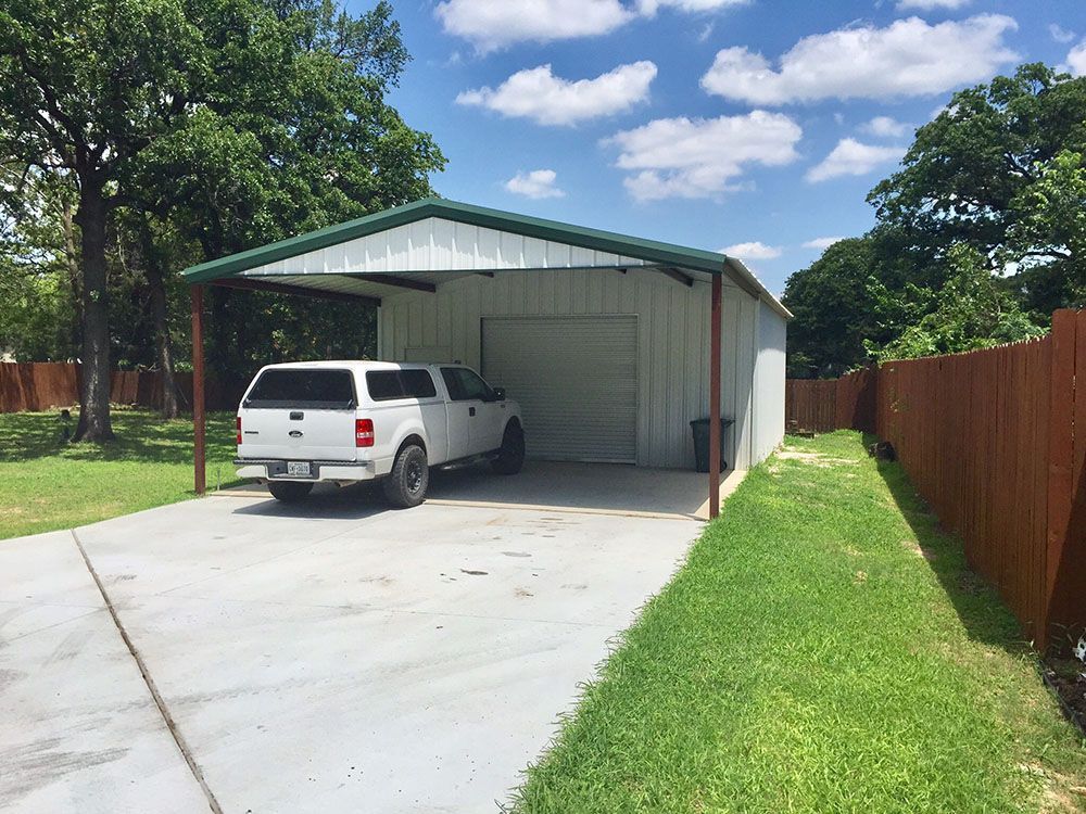 A white truck is parked under a carport in a driveway.