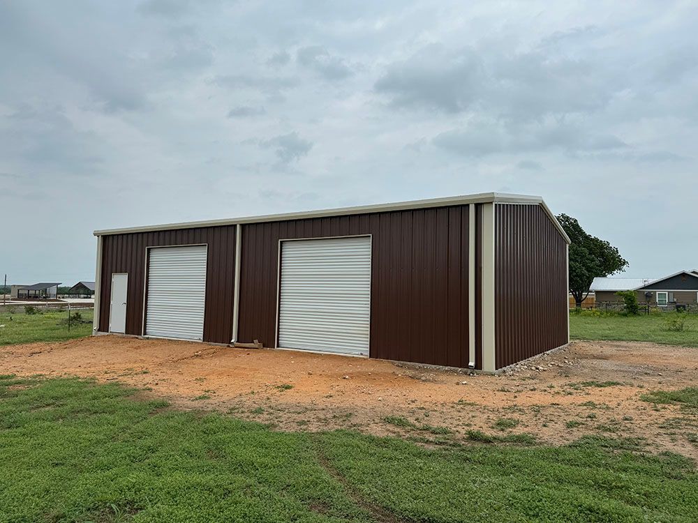 A brown and white metal building is sitting in the middle of a grassy field.