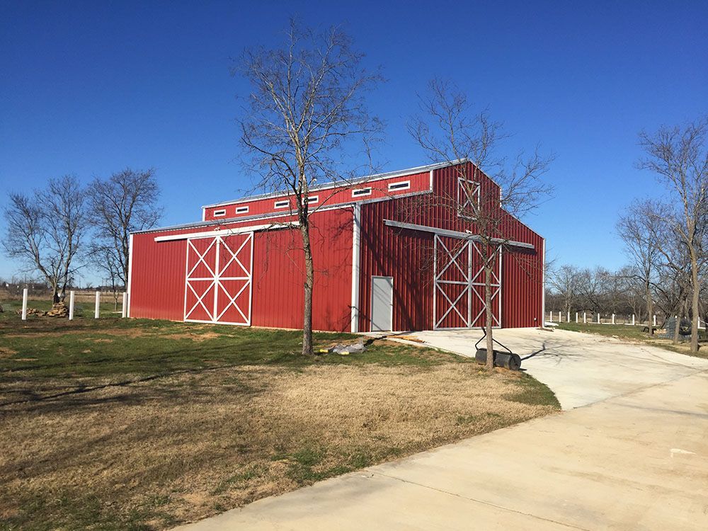A large red barn is sitting in the middle of a grassy field.