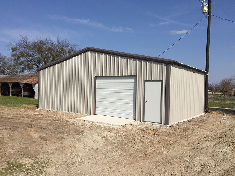 A metal garage with a white garage door is sitting in the middle of a dirt field.