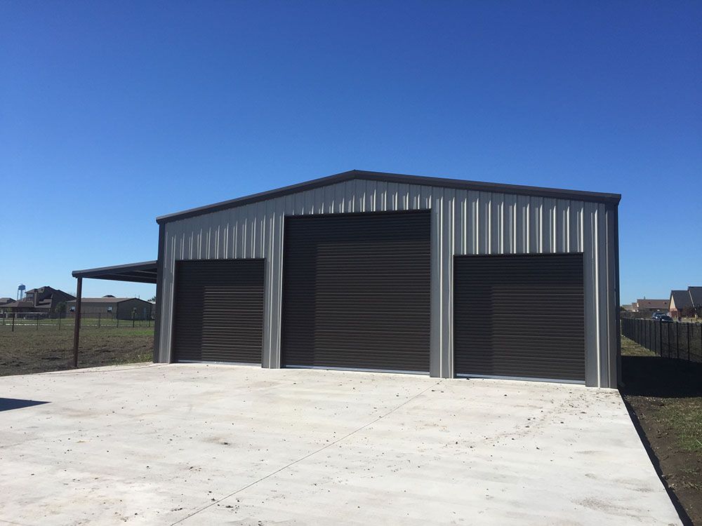 A metal garage with three garage doors and a concrete driveway.
