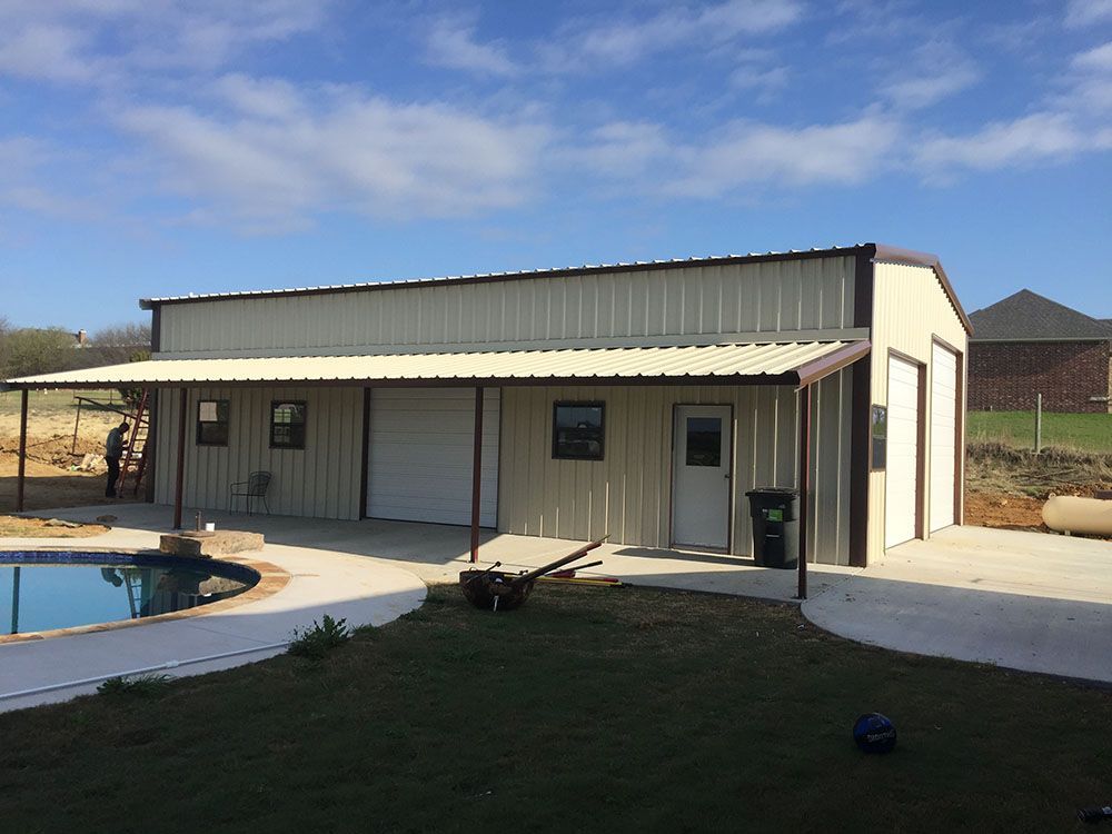 A metal building with a porch and a garage next to a pool