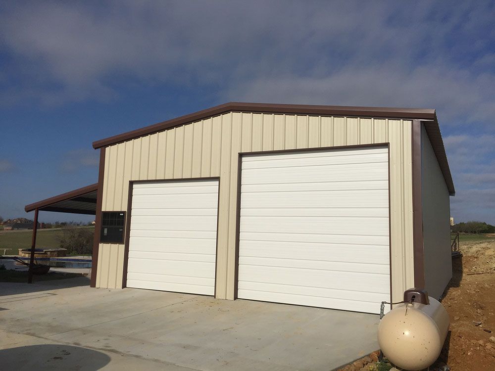 A garage with two white garage doors and a propane tank in front of it