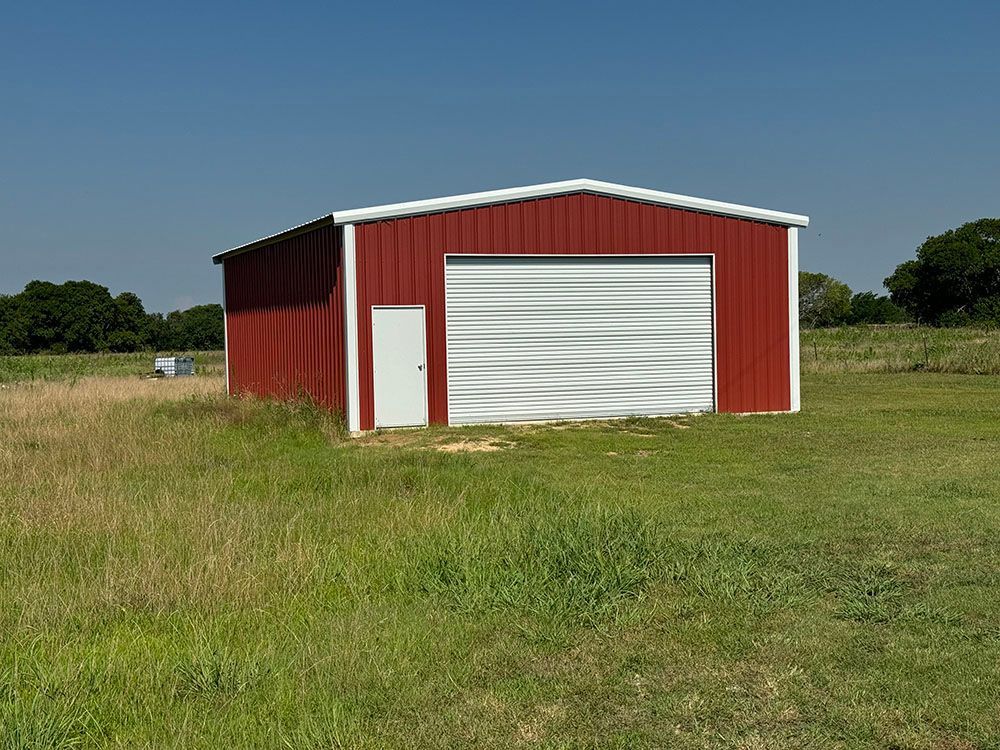 A red barn with a white door is in the middle of a grassy field.