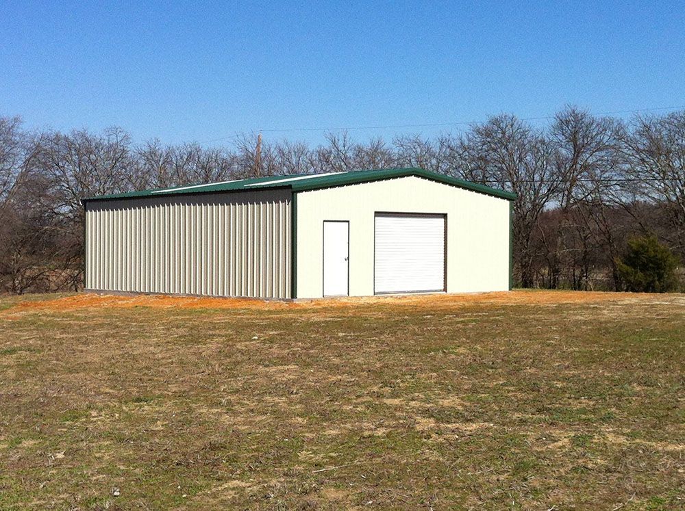 A white building with a green roof is in the middle of a field.