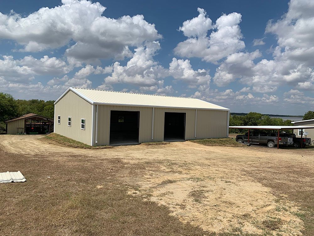 A large metal building with two garage doors is sitting in the middle of a dirt field.
