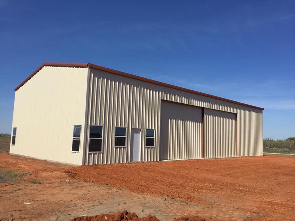 A large white building with a red roof is sitting in the middle of a dirt field.