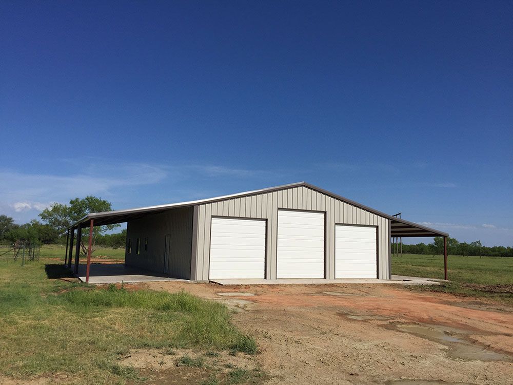 A metal building with three garage doors and a canopy in a field.