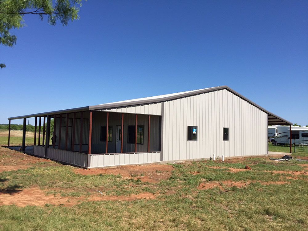 A large metal building with a screened in porch is sitting in the middle of a grassy field.