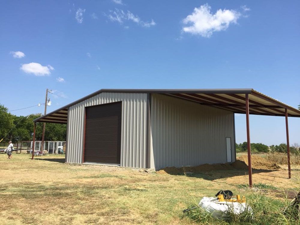 A large metal building with a canopy is sitting in the middle of a field.