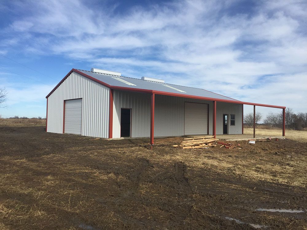 A large metal building with a red roof is sitting in the middle of a dirt field.
