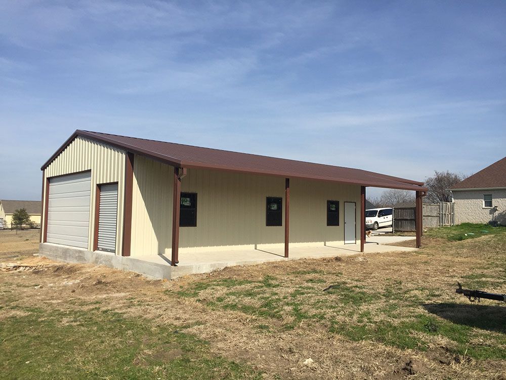 A large metal garage with a porch and a truck parked in front of it.