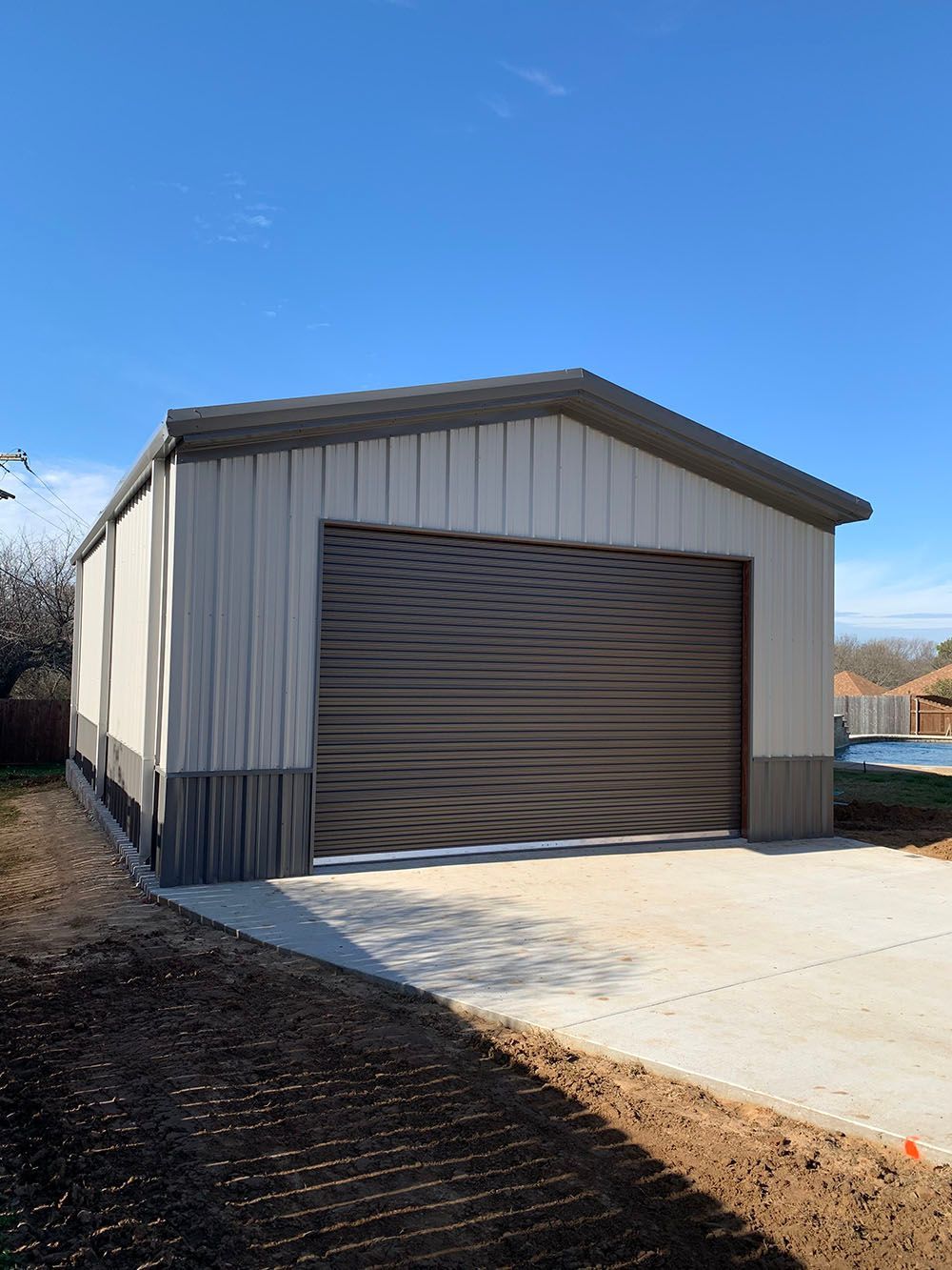 A metal garage with a concrete driveway in front of it.