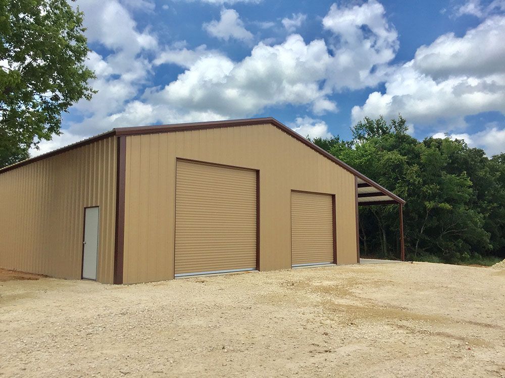 A large metal building with two garage doors is sitting in the middle of a dirt road.