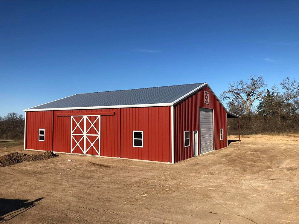 A large red barn is sitting in the middle of a dirt field.