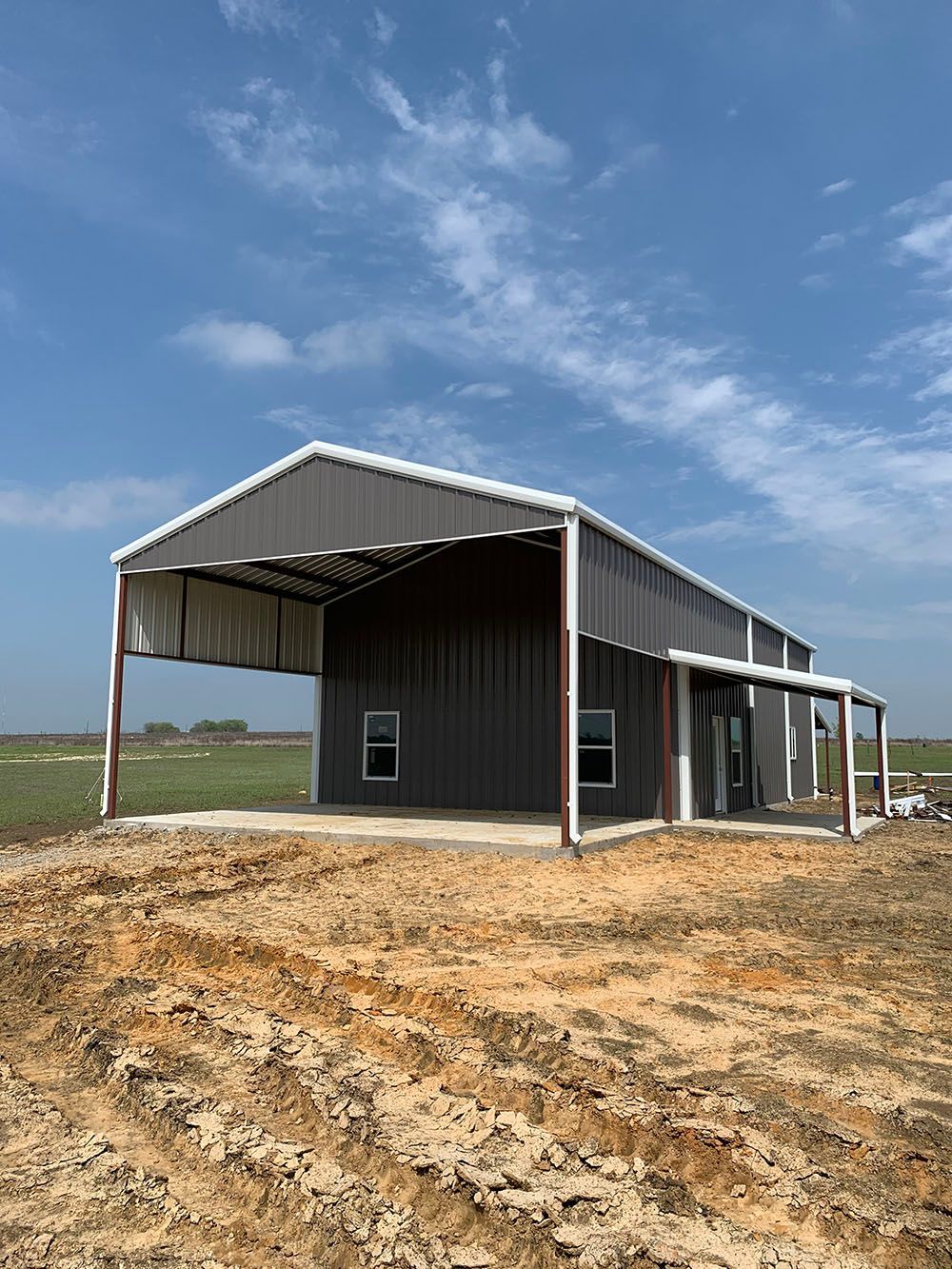 A metal building with a porch is sitting in the middle of a dirt field.