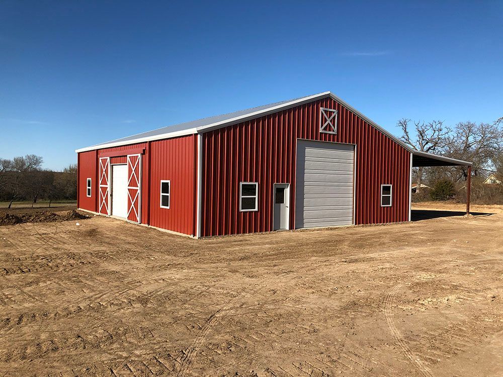 A large red barn is sitting in the middle of a dirt field.