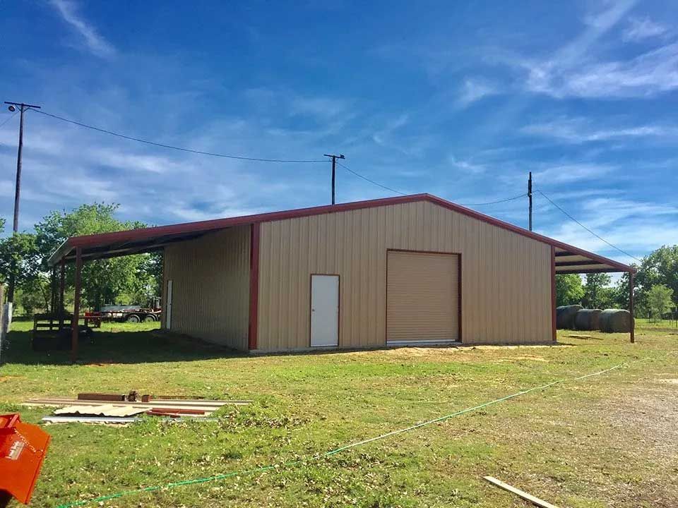 A large metal building with a red roof is sitting in the middle of a grassy field.