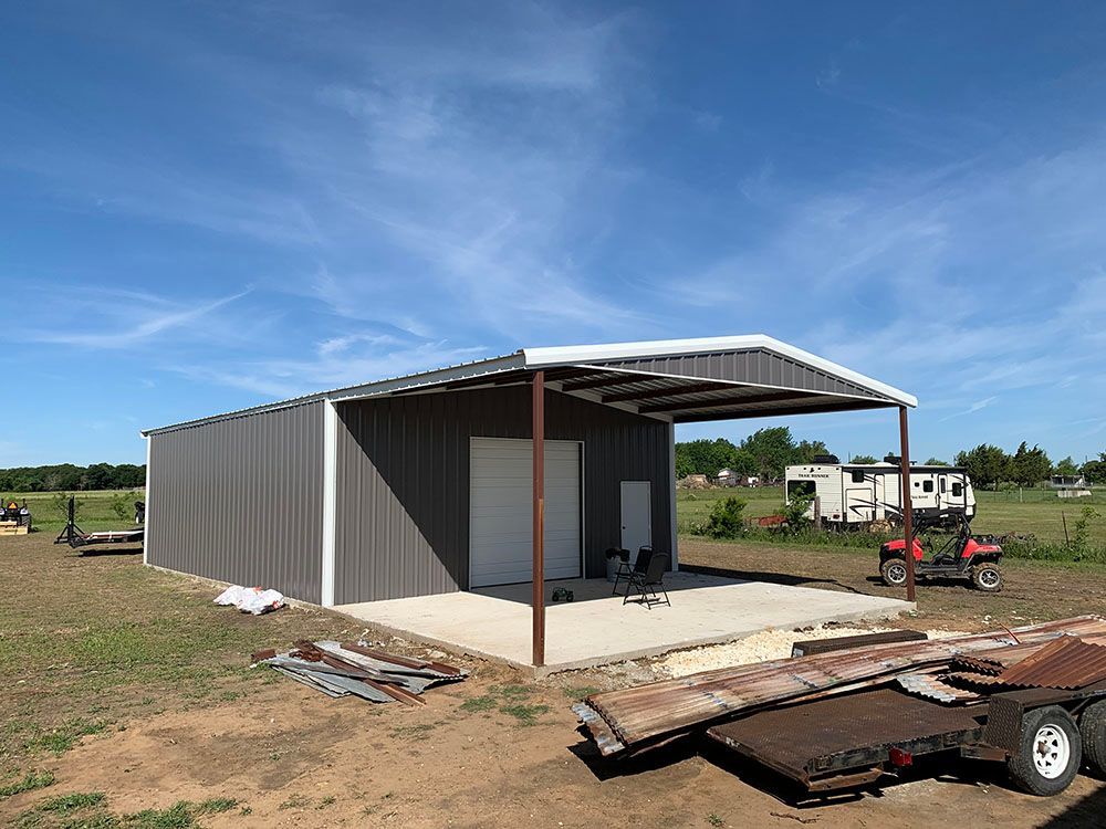A metal building is being built in a field next to a trailer.