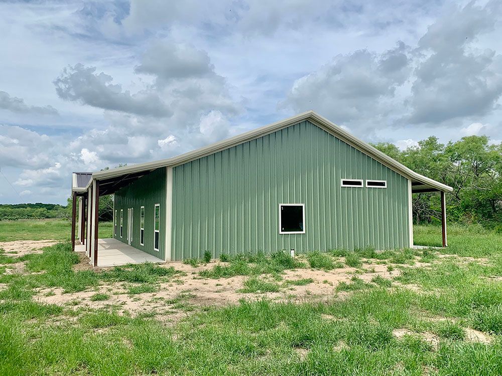 A green metal building is sitting in the middle of a grassy field.