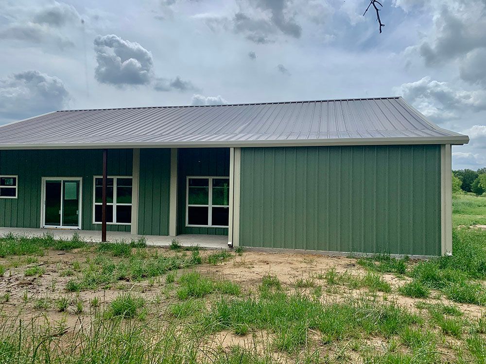 A green building with a gray roof is sitting in the middle of a grassy field.
