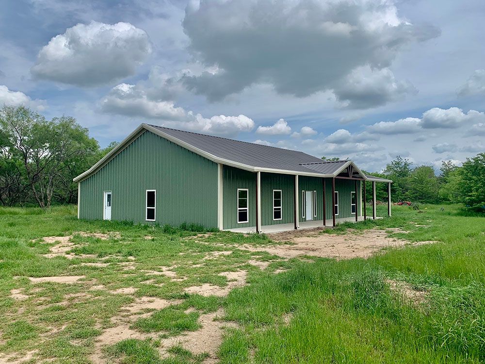 A green building with a porch is sitting in the middle of a grassy field.