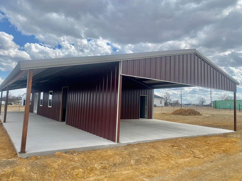 A large metal building with a covered parking lot in the middle of a field.
