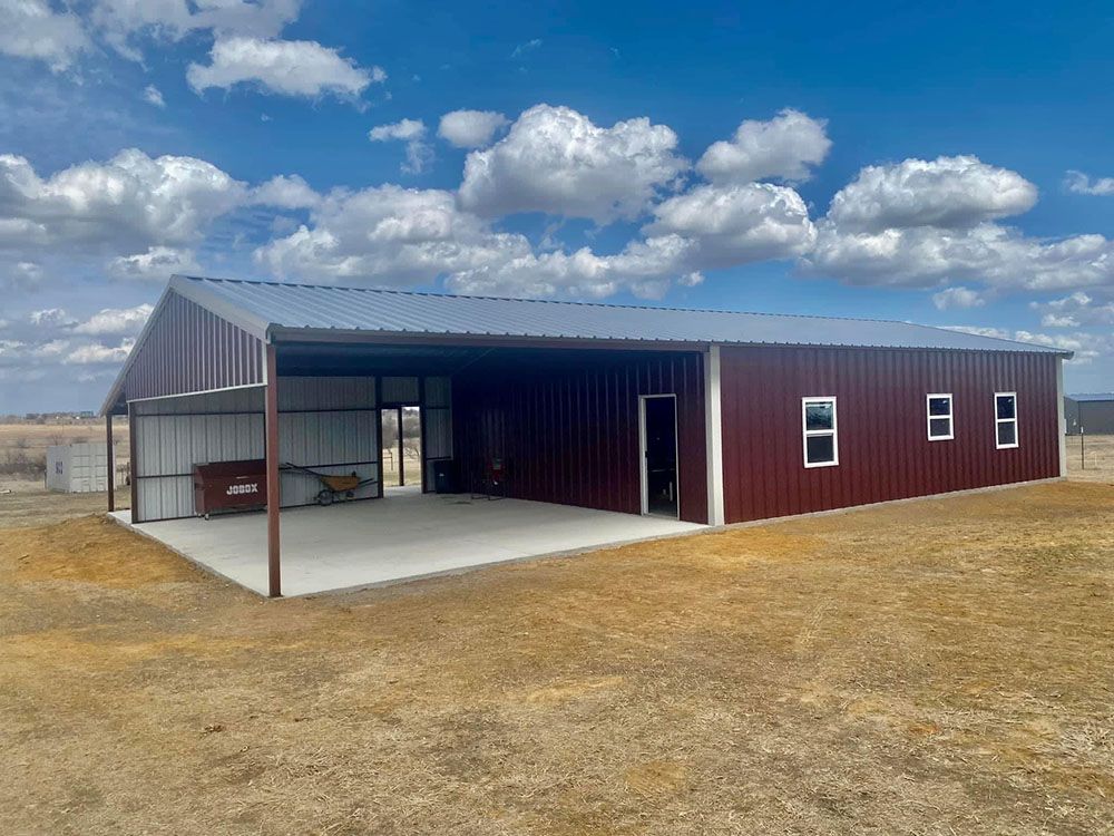 A large red metal building with a covered porch in the middle of a field.