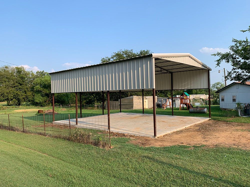 A metal carport is sitting in the middle of a grassy field.