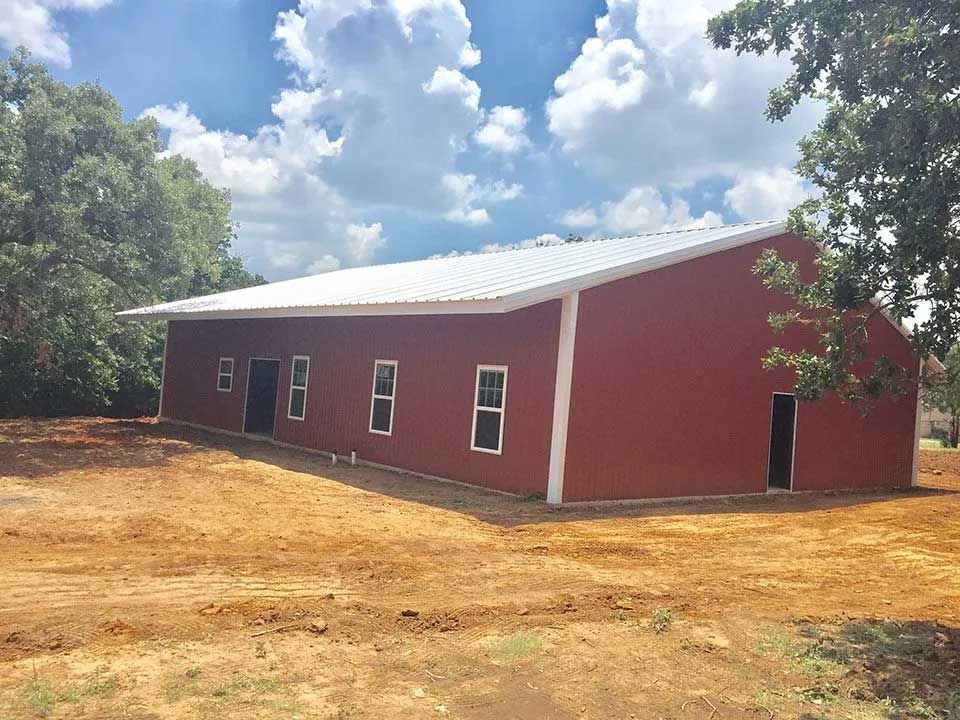 A large red barn is sitting in the middle of a dirt field.