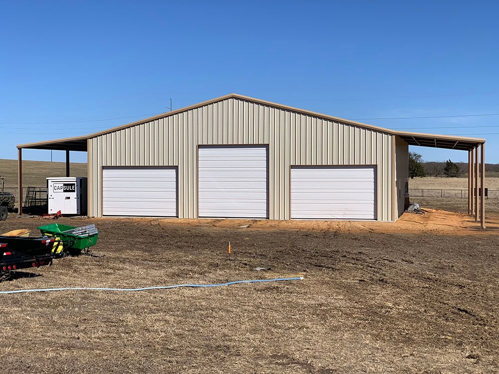 A large metal building with three garage doors is being built in a field.