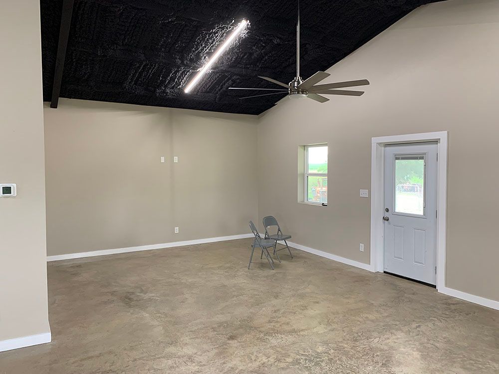 A large empty room with a ceiling fan and a door.